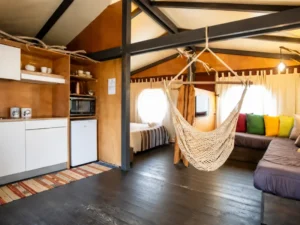 Intérieur spacieux d'un hébergement glamping au Wind Resort à Lo Stagnone en Sicile avec cuisine équipée, salon et hamac.