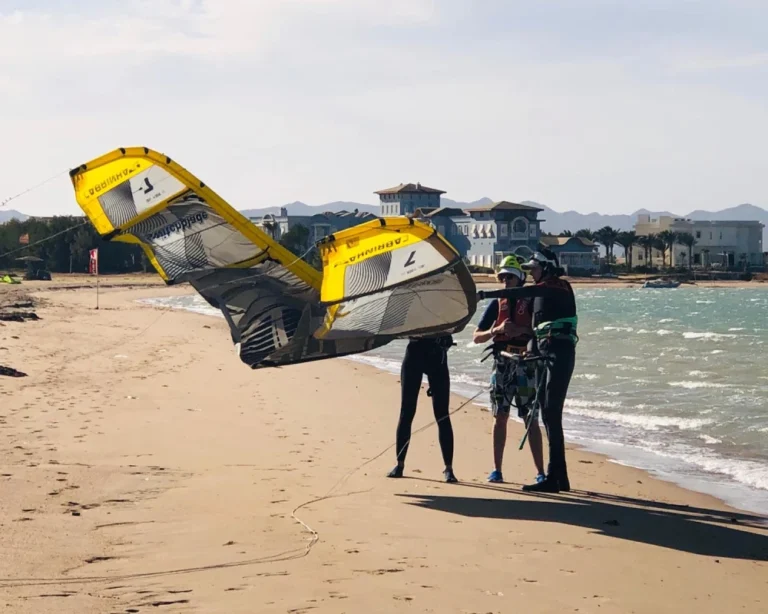 Een KiteTrek-instructeur begeleidt twee cursisten bij het voorbereiden van de kite vóór een kitesurfles in Zeeland.